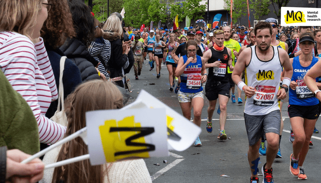 Runners running a charity run for MQ are being waved on by supporters waving MQ flags