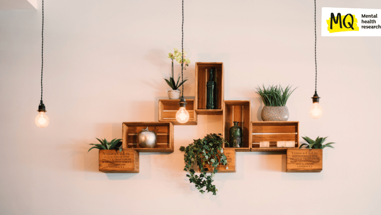 On a white wall wooden rectangular shelves hold attractive plants and 3 industrial lightbulbs hang from the ceiling above