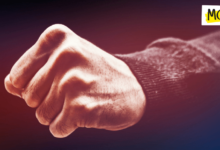 A clenched fist is pictured close up with a burgundy shirt on the wrist against a dark background.