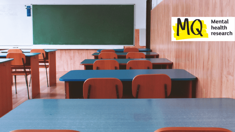 Rows of empty school desks face a green blackboard in a schoolroom as if we are sitting in the classroom looking to the front of class