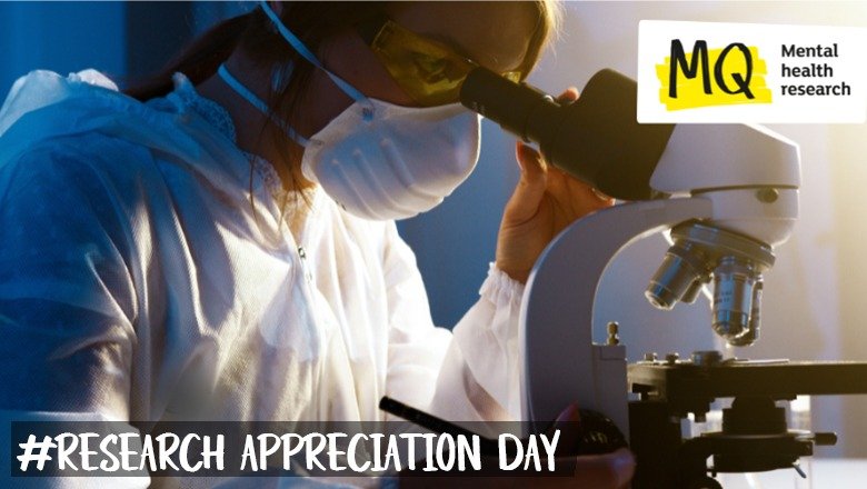 A female presenting scientist wears a face mask as she looks into a microscope with dramatic lighting