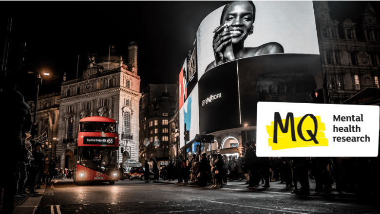 London at night. A red double decker bus drives past large lit up billboards full of advertisements