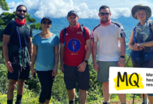 5 trek participants stand in front of beautiful background of jungle and blue skies in the sunshine. Mark Drain, the interviewee in this article, stands in the centre.